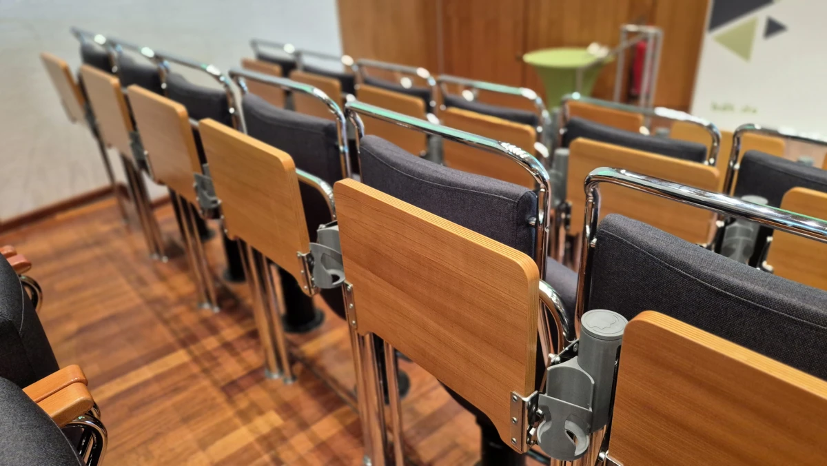 Reihen moderner Konferenzstühle mit Holzrückenlehnen und gepolsterten Sitzen im hdt Congress Center, seitliche Ansicht eines Seminarraums.