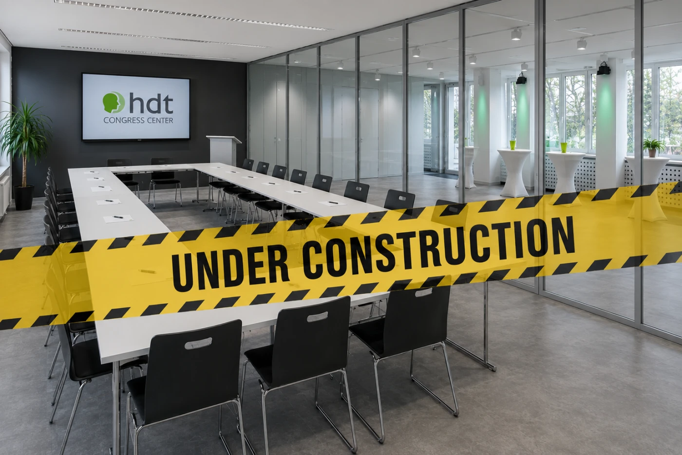 Visualisierung eines modernen Seminarraums im hdt Congress Center während der Bauphase. Der flexibel teilbare Raum verfügt über eine Glastrennwand, moderne Konferenztische in U-Form, ein großes Wanddisplay und eine hochwertige Ausstattung. Ein gelbes „UNDER CONSTRUCTION“-Banner weist darauf hin, dass sich der Seminarraum derzeit noch im Ausbau befindet.